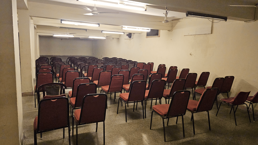 An indoor conference hall filled with rows of maroon padded chairs facing forward under warm fluorescent lighting.