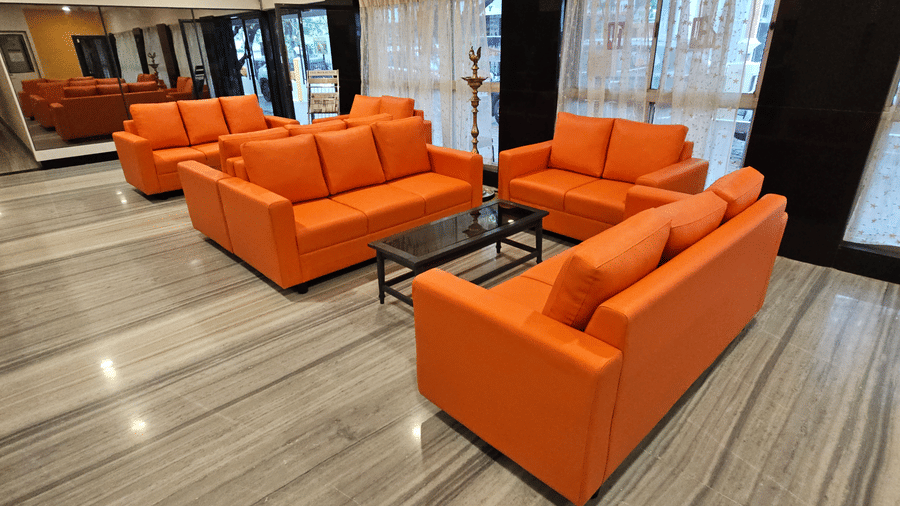 A hotel lobby seating area featuring multiple bright orange sofas arranged around a dark coffee table on a polished marble floor - Hotel Pandian