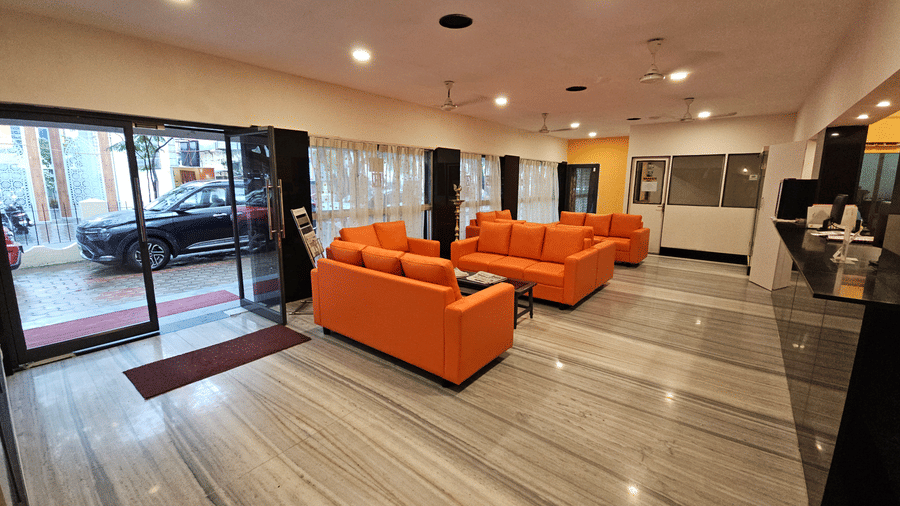 A spacious lobby entrance area showing orange seating arrangements, glass doors leading outside to a parked car, and bright ceiling lighting - Hotel Pandian