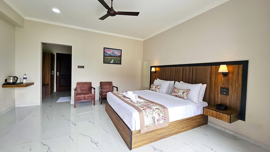  A bright and inviting bedroom at Yashshree Resort & Spa Kalimpong features a large bed, two armchairs, a small table with a kettle, and a ceiling fan.