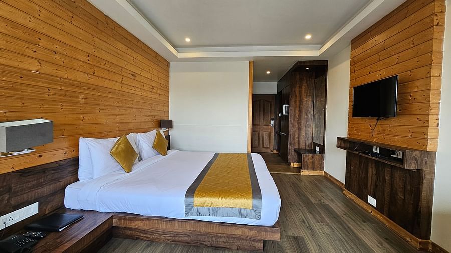 An image of a deluxe room with a bed, bed side table, lamps, and flat screen TV - Yashshree Sanderling, Darjeeling