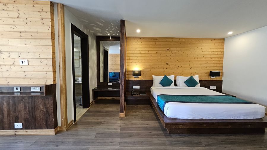 An image of a deluxe suite showcasing the bedroom with bed, bed side table, lamps, and doors leading to the other parts of the suite - Yashshree Sanderling, Darjeeling