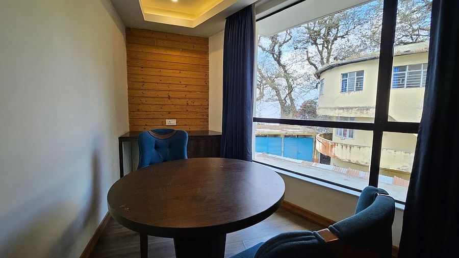 An image of a deluxe suite showcasing two chairs, a round wooden table, and an expansive window - Yashshree Sanderling, Darjeeling