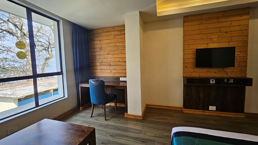 An image of an executive premium room with a flat screen TV, work desk, chair and an expansive window overlooking the view - Yashshree Sanderling, Darjeeling