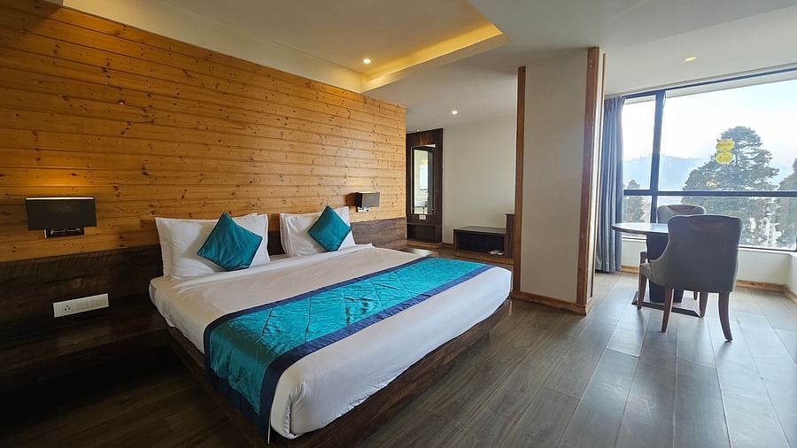 An image of a premium suite with a bed, bed side table, lamps, a table, two chairs, and an expansive window - Yashshree Sanderling, Darjeeling