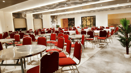 A large, bright banquet hall is filled with round dining tables and striking red chairs.