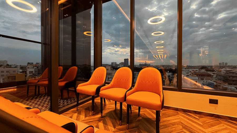 3 chairs paced in the restaurant overlooking the cloudy evening skies in the background from the huge windows at F Hotels, Bengaluru.