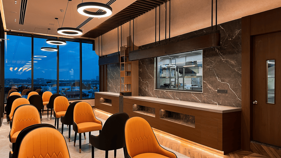 A wide-angle shot of the restaurant featuring several cushioned chairs placed facing each other with a buffet counter at F Hotels, Bengaluru.