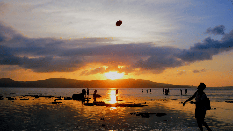 Silhouettes of people are enjoying a scenic beach sunset, with one person kicking a ball in the air.