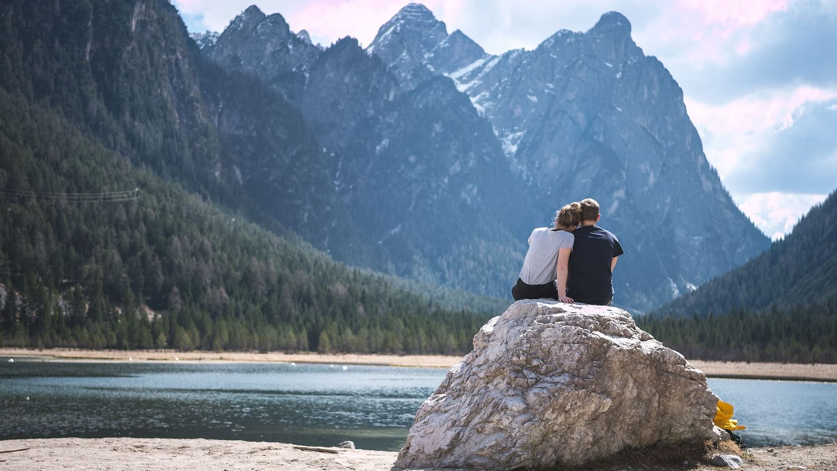 A couple sitting on a massive rock overlook to mountains