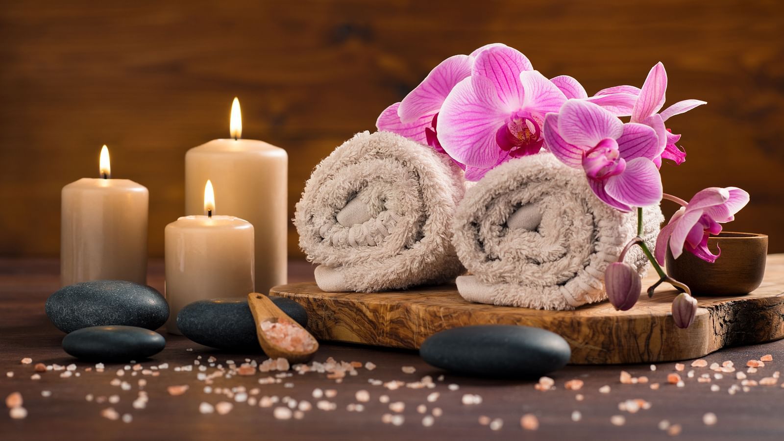 spa-setting-with-brown-rolled-towel-orchids-candles-wood