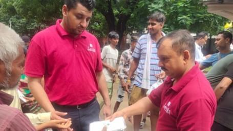 People in red shirts are distributing food and drink to a group of men in a street - Lords Hotels & Resorts