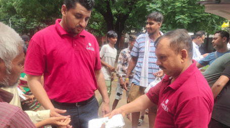 People in red shirts are distributing food and drink to a group of men in a street - Lords Hotels & Resorts