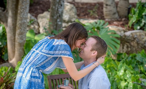 A woman in a blue and white dress leaning to kiss a man seated outdoors amid lush greenery at Casa Morada.