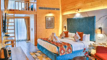 A cosy room with wooden paneling, a plush bed with a blanket on it, and warm lighting.- Bamboo Saa Resort & Spa, Udaipur.