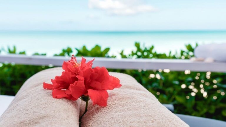 A close-up of folded towels with a red flower placed on them, overlooking a serene ocean view.