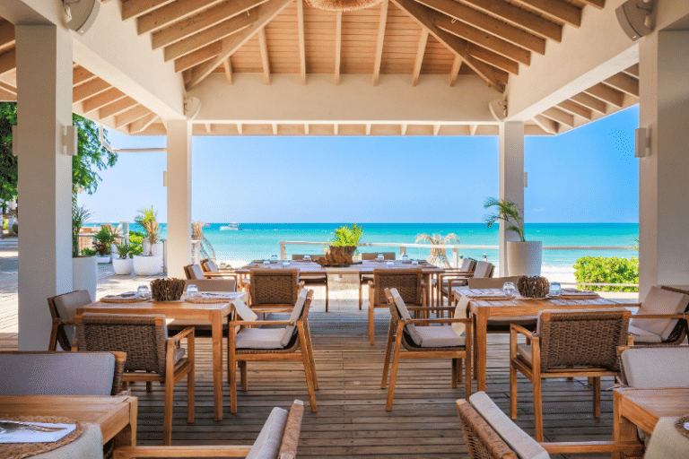 An open-air restaurant with wooden tables and chairs, offering panoramic views of the ocean and clear sky at the Tamarind Hills Resort and Villas - Antigua.