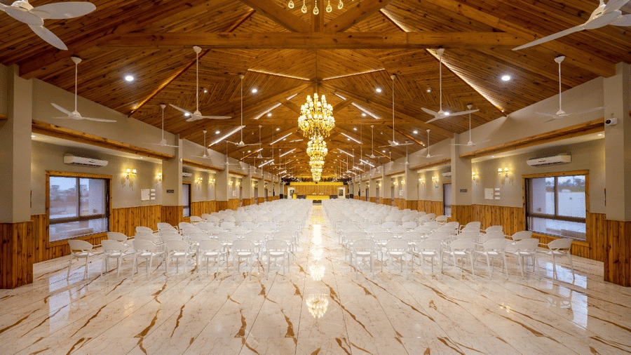 A wide view of a large banquet hall with numerous tables and chairs set under ornate lighting at Angel Lords Eco Inn Amreli.