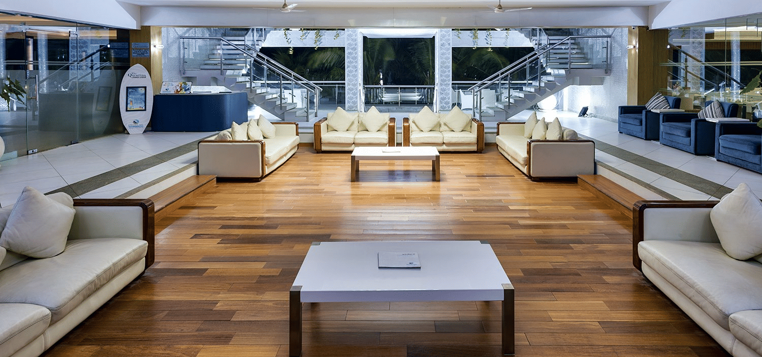 An indoor lobby area with white sofas, chairs, coffee tables, and large windows at Grande Bay Resort & Spa, Mamallapuram.