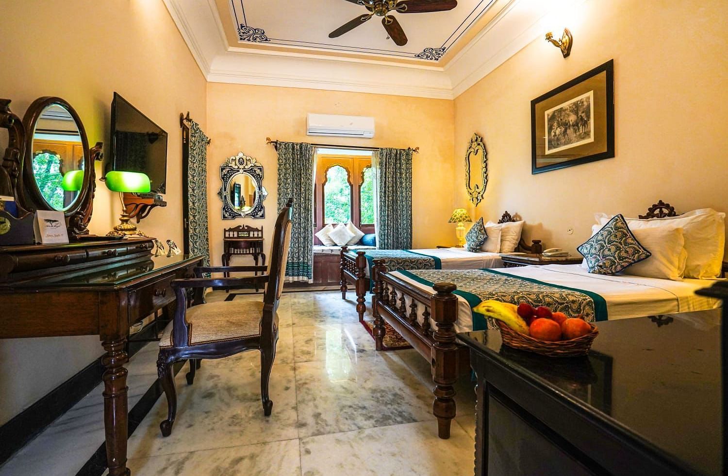 A spacious and elegant hotel room with twin beds and a fruit platter set on the table - Khas Bagh, Jaipur.
