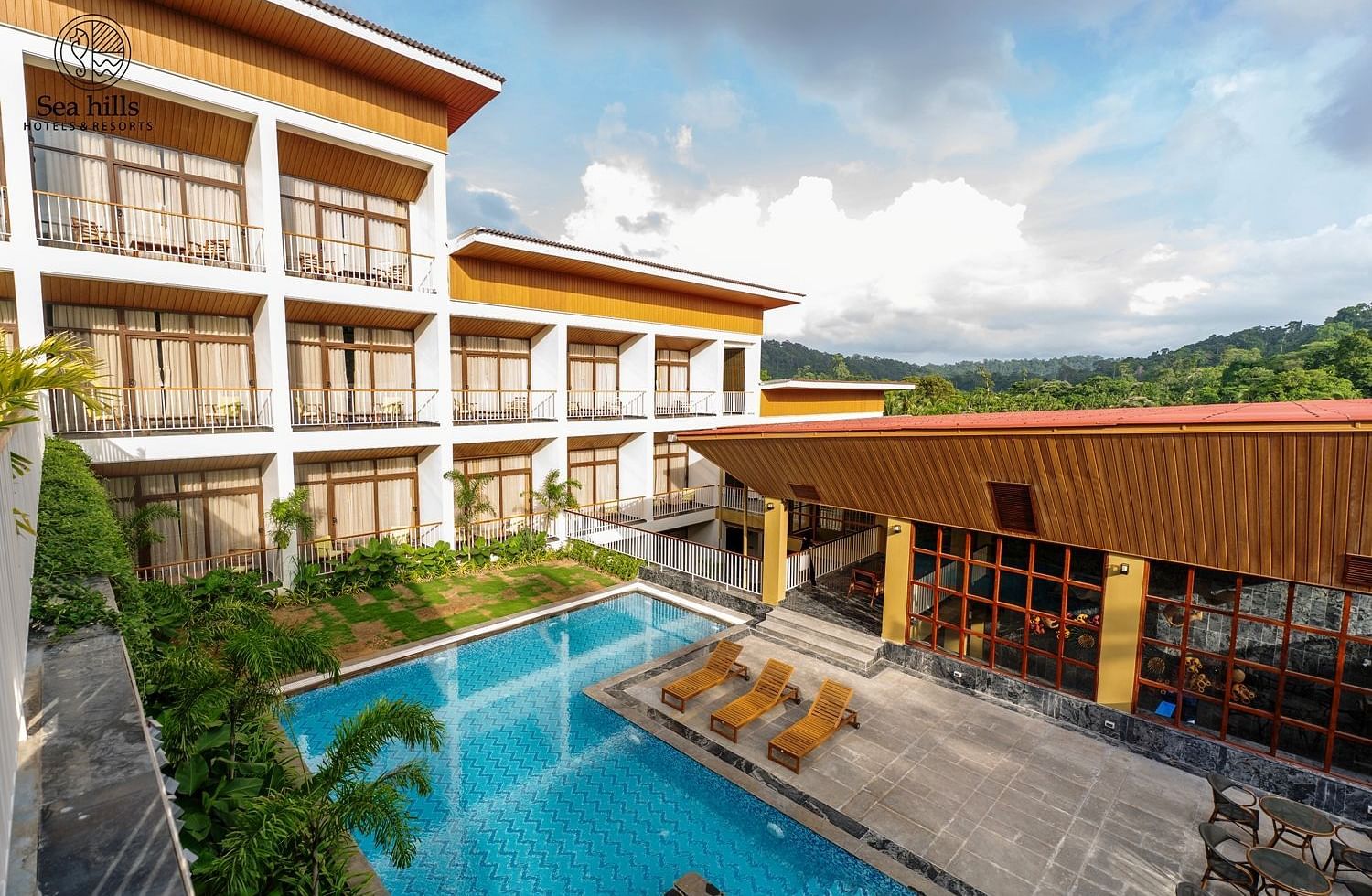An exterior shot of a large resort building with multiple floors and an outdoor swimming pool, set against a hilly landscape. - Sea Hills Resort, Swaraj Dweep (Havelock)