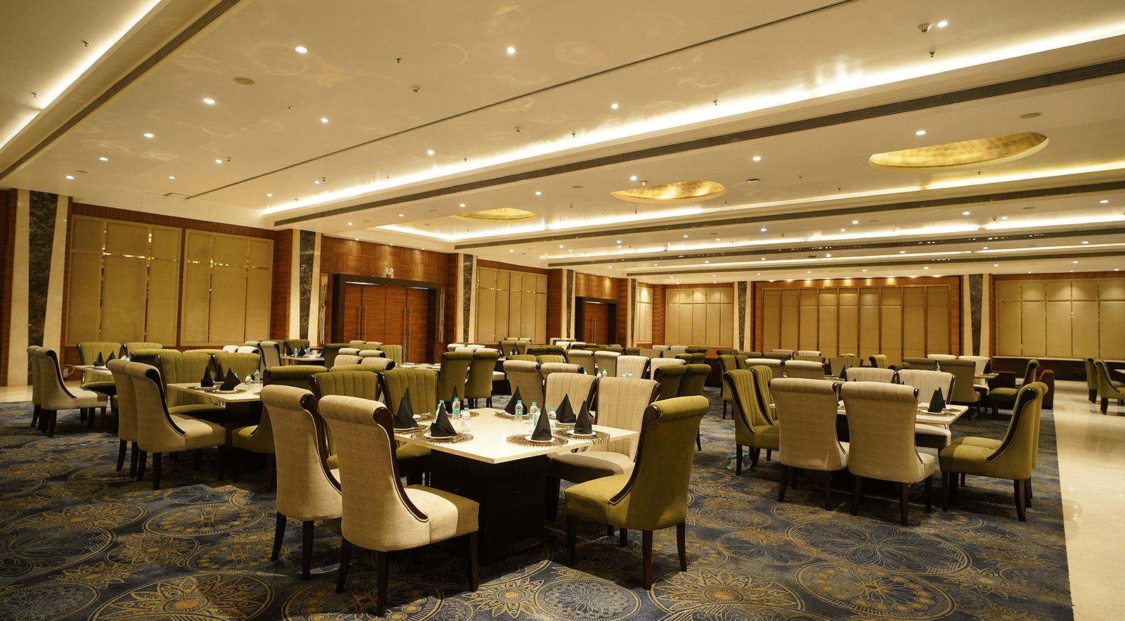 A spacious and modern banquet hall at Nirvana Luxury Hotel, Ludhiana, set with neatly arranged tables and chairs on a patterned blue carpet, ready for an event.