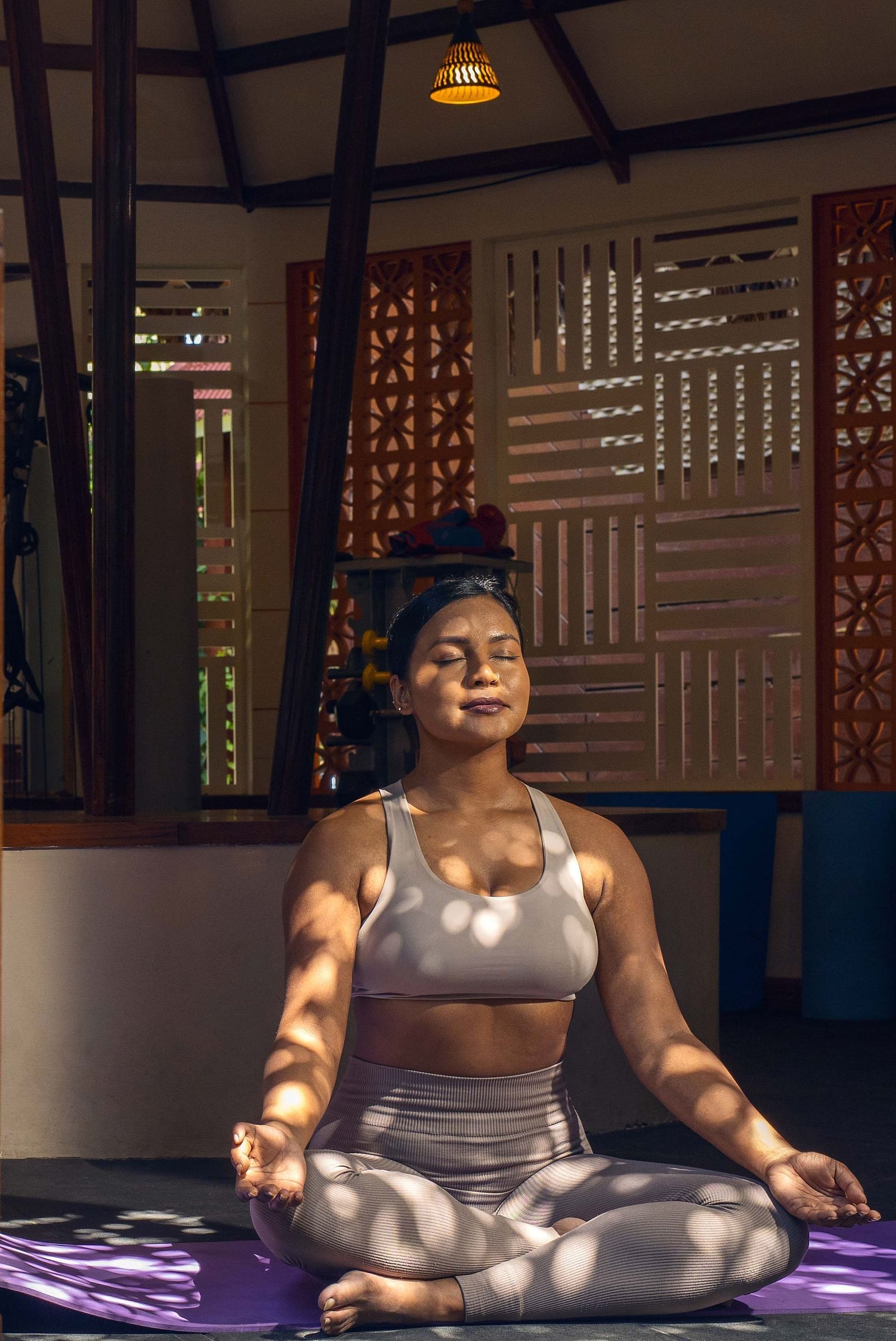 A portrait shot of a  woman meditating in a peaceful shady room, on a yoga mat.