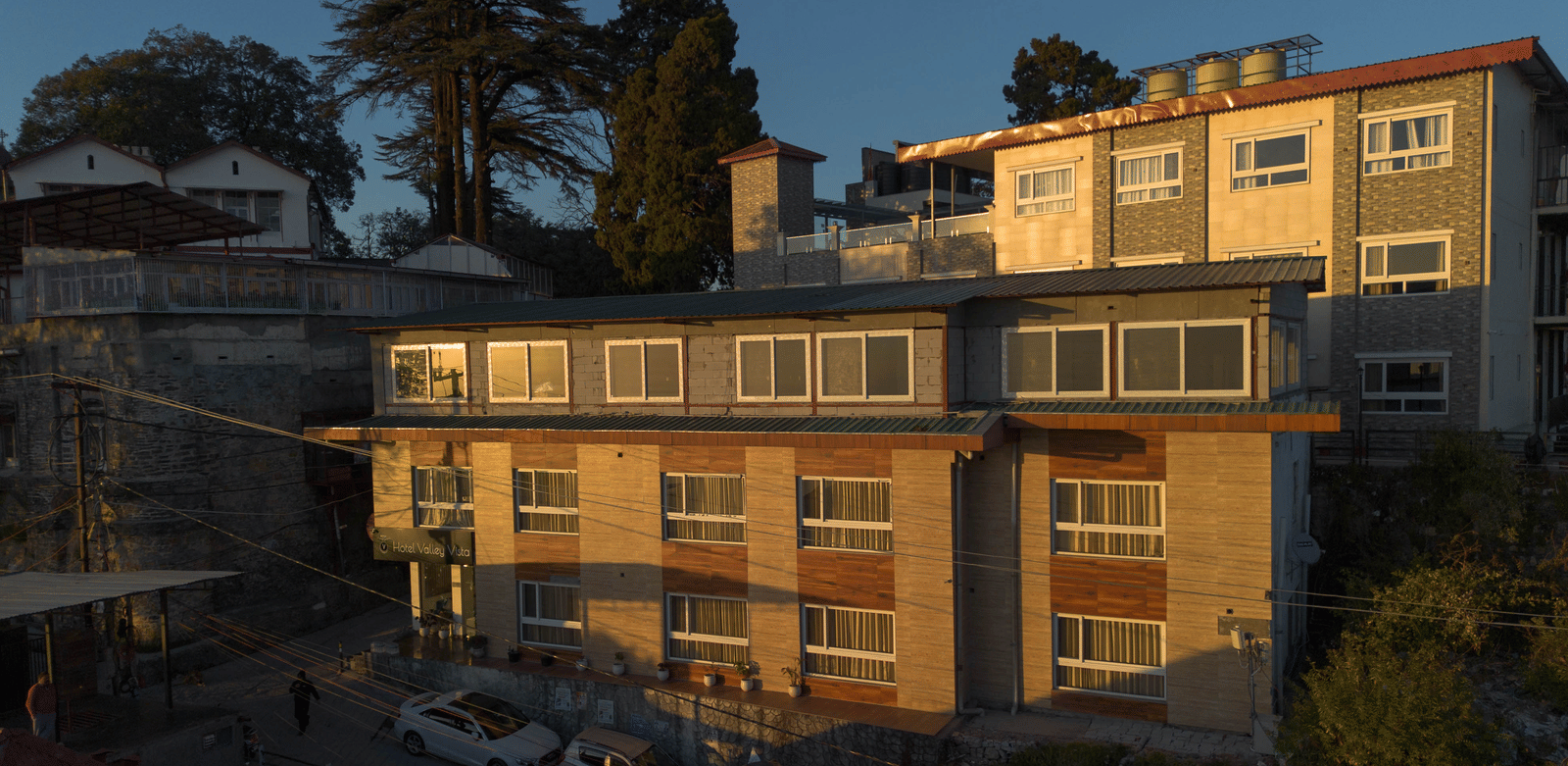 The exterior of a multi-story hotel building with balconies, built on a hillside and illuminated by evening light | Perfectstayz Value Valley Vista