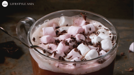 Rich hot chocolate topped with pink and white marshmallows and chocolate shavings, served in a glass mug.