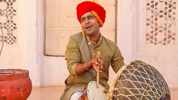 A person playing a traditional drum, sitting on the floor.