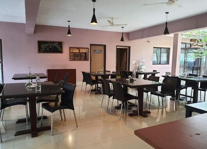 The spacious dining room at Paradise Wild Hills Resort, Kollur, with multiple tables and chairs ready for guests.