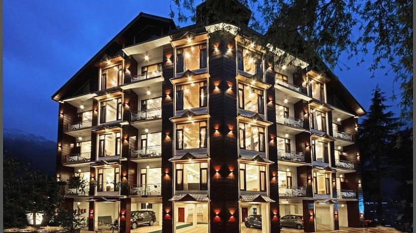 A large, multi-story hotel building illuminated at night, with a mountain backdrop | DLS La Serene Manali