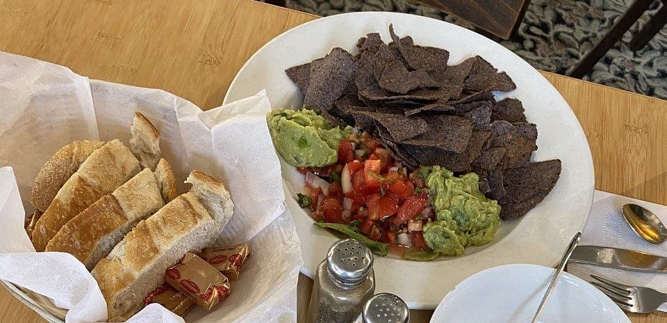 Two plates of food on a table, one with a stew along with shells and the other with a dish of sliced meat.