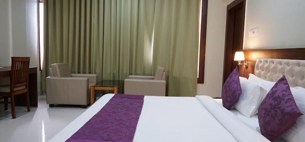 A well-lit room with plush seating, purple bedding, and floor-length curtains creating a calm atmosphere - Pemaling Lords Eco Inn Guwahati