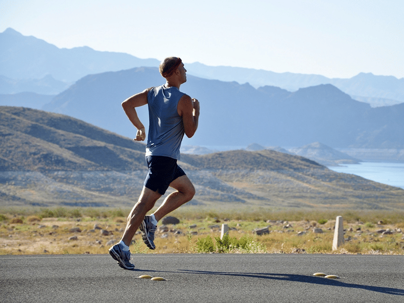 A man running along a road with mountains and a lake in the background
