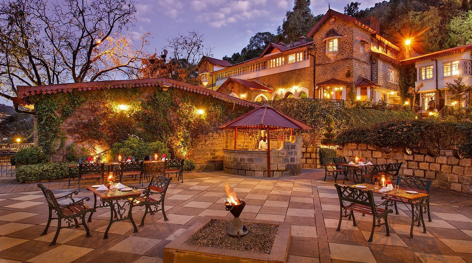 Hotel facade illuminated with warm lighting, and a few tables arranged in the evening.
