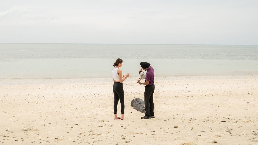 Man and woman standing together on a wide, sandy beach near the calm ocean under an overcast sky.