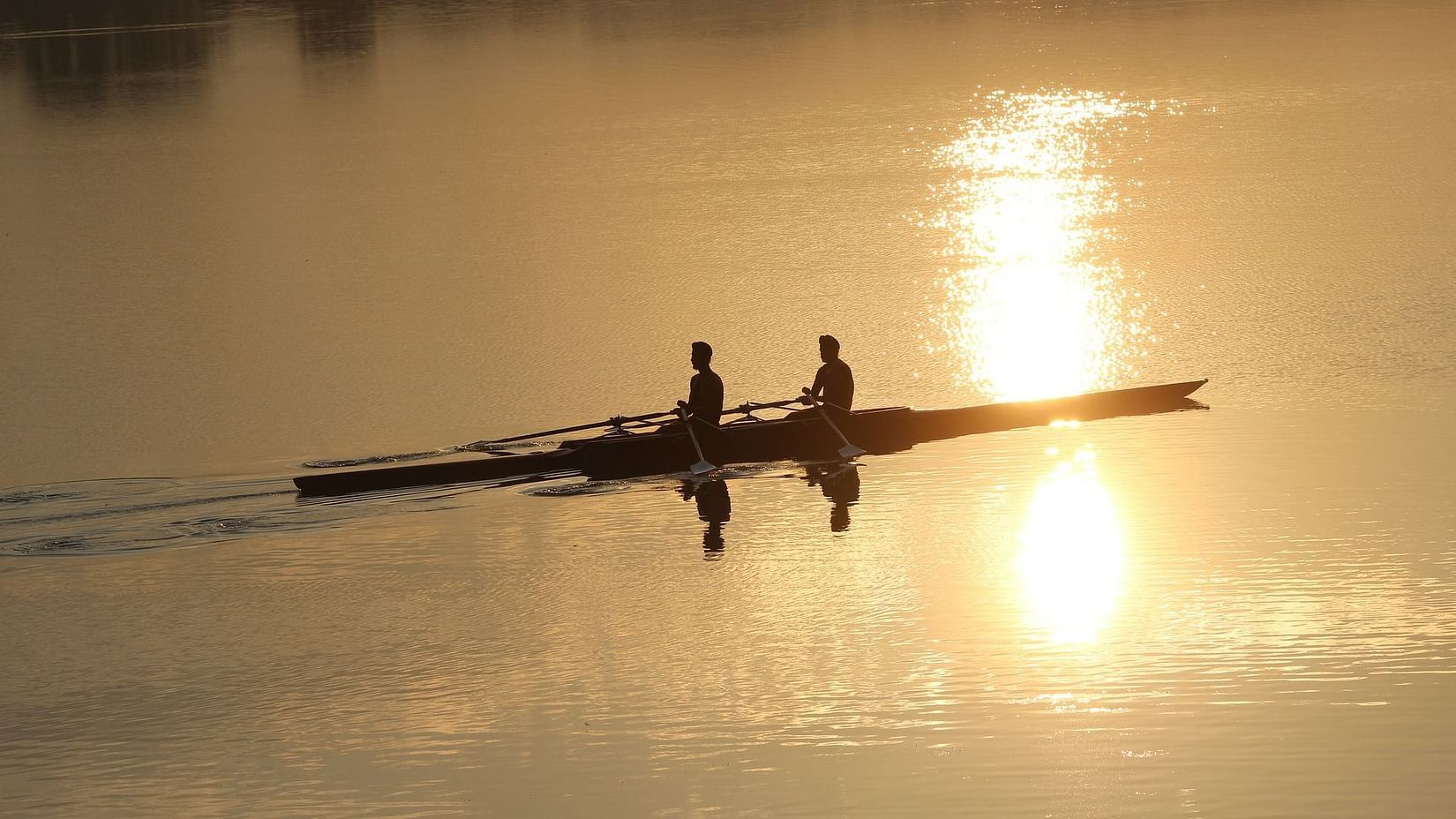 Two people rowing a boat on a lake with sun light reflecting on the water
