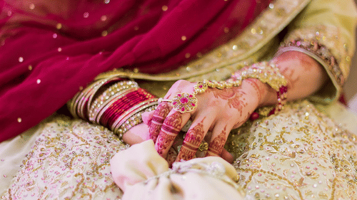 A bride resting her hands on her lap, adorned with intricate jewellery and henna, during a wedding.