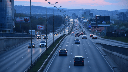 Aerial view of a city highway with vehicles in motion under an orange evening sky.