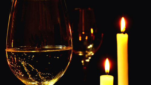 A wine glass with white wine and two candles