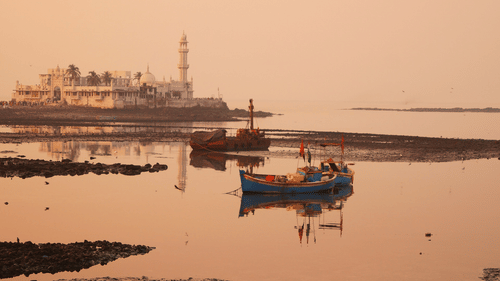 A view of a mosque on the shore with boats floating on the water during hazy weather.