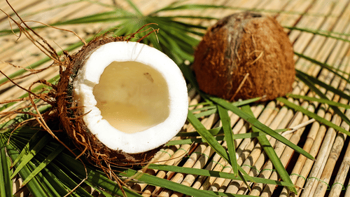 A halved coconut placed on palm leaves on a mat.