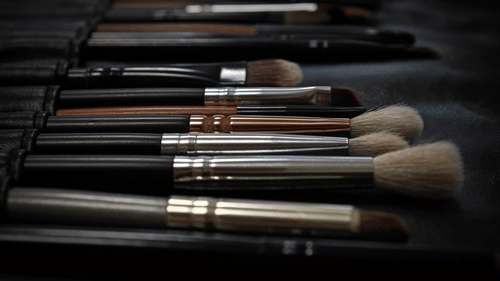 A set of various makeup brushes with different head shapes and sizes are arranged in rows within a dark case or holder.