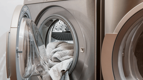 A silver front-loading washing machine with its door open displays clothes inside the drum, placed beside a matching appliance.