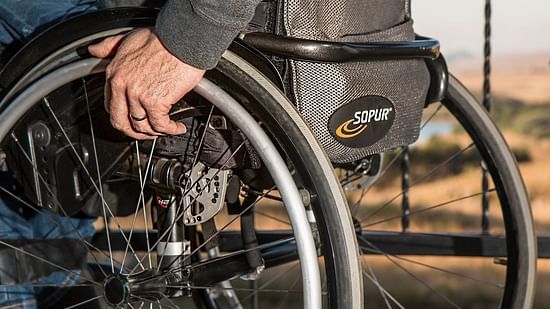 A person's hands propel a wheelchair forward, focusing on the wheels and the individual's grip, with a blurred outdoor background.