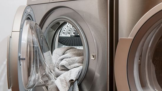 A silver front-loading washing machine with its door open displays clothes inside the drum, placed beside a matching appliance.