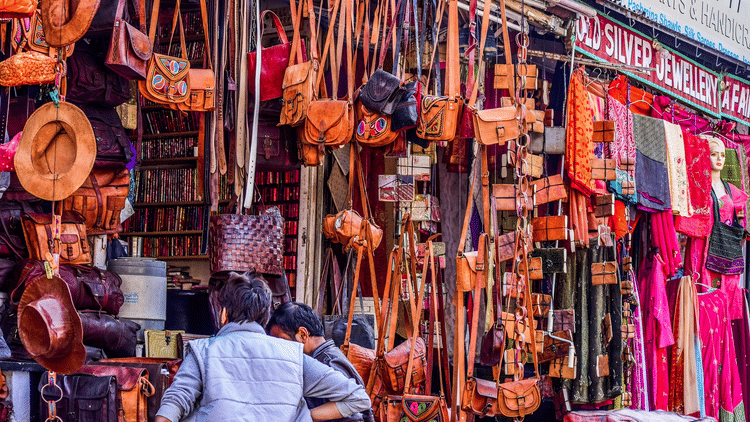 visitors looking inside a street shop that is selling leather bags 