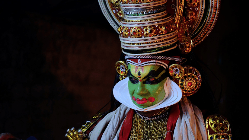 A Kathakali dancer with their attire on against a dark background