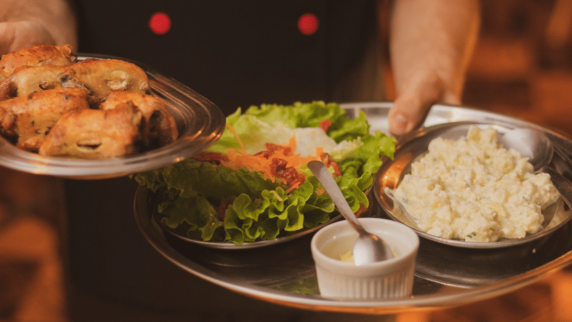 A server holding a tray with plated food and side dishes.